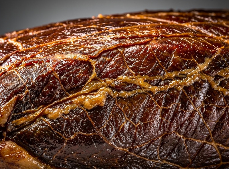 Macro detail of dry-aged crust pellicle on a beef subprimal showing dark amber color and dry leathery surface texture