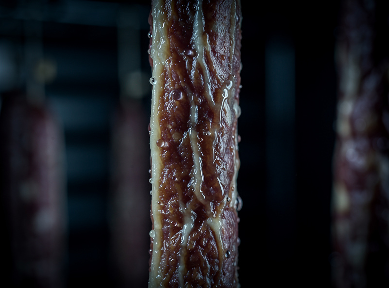 Macro of a dripping cured salami casing showing slimy wet surface and beads of water from chamber humidity overshoot