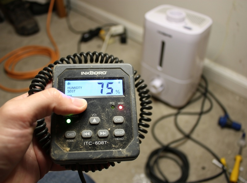 Hand adjusting Inkbird ITC-608T humidity controller display showing setpoint at 75 percent with humidifier unplugged on the floor
