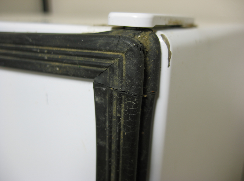 Worn and cracked rubber door gasket on a white mini fridge with a visible flat spot at the corner where the seal has compressed permanently