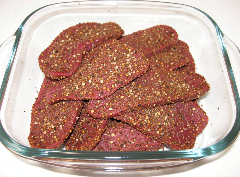 Beef strips fully coated in coarse coriander and cracked pepper spice rub resting in a glass dish ready to cure