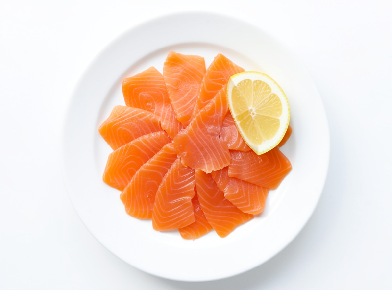 Thinly sliced cold-smoked salmon arranged on a plate with lemon
