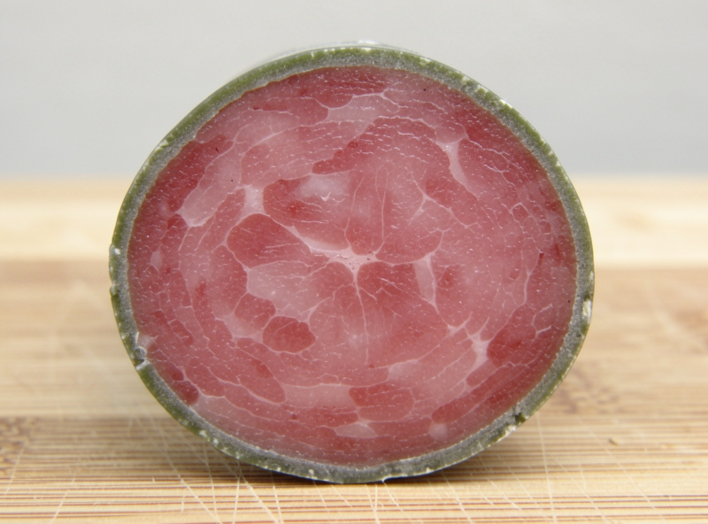 Cross-section of fermented dry-cured sausage with a rosy cured core and a thin discolored outer ring