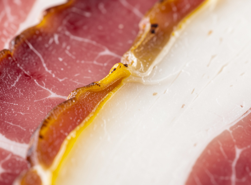Macro close-up of sliced cured meat with yellowed oxidized fat edges next to creamy white fat