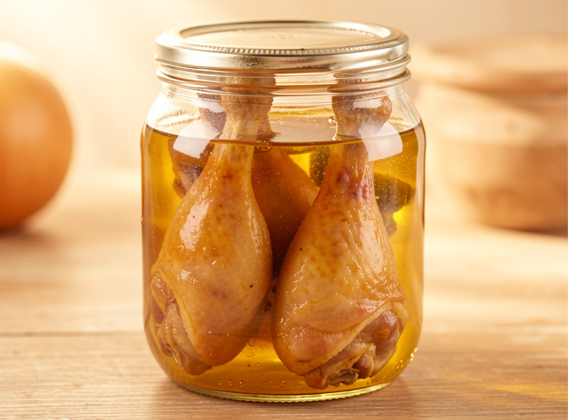 Cooked duck legs submerged in golden fat in a jar, stored confit