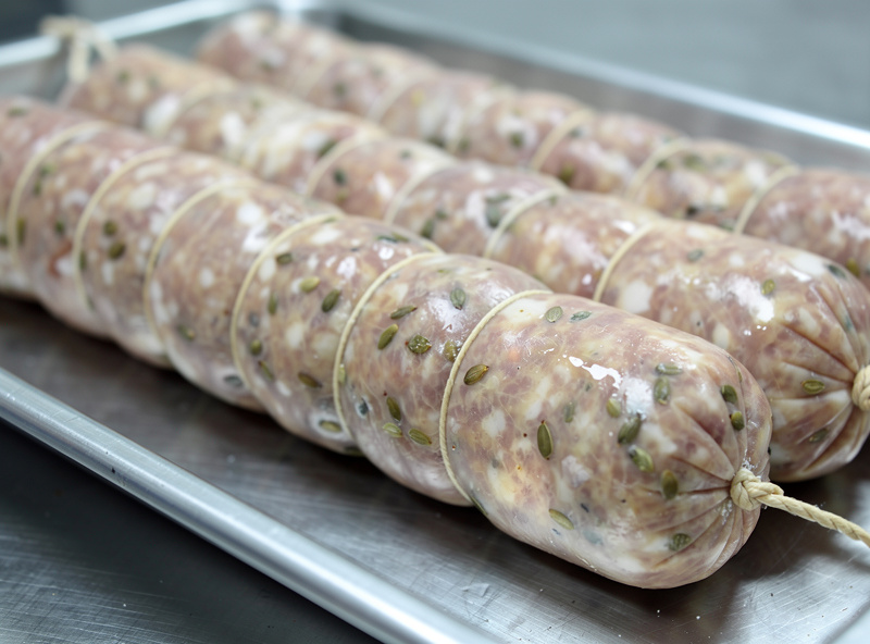 Freshly stuffed finocchiona salami in natural casings tied with twine, whole fennel seeds visible through the translucent casing