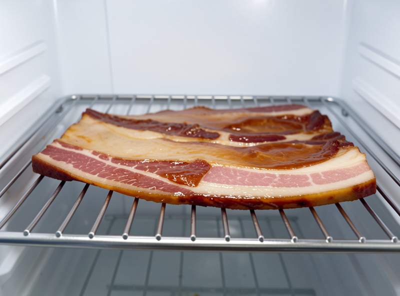 Cured pork belly resting uncovered on a wire rack in a fridge forming a glossy pellicle before slicing