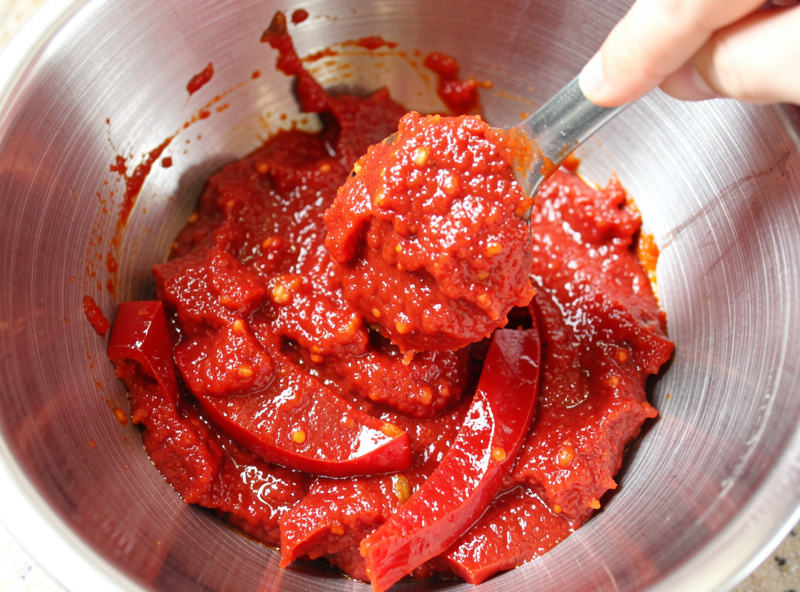 Bright red 'nduja paste being mixed with Calabrian chili in a chilled stainless bowl