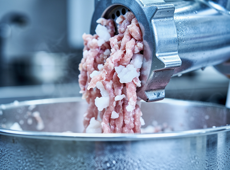 Coarse-ground pork and white fat extruding from a meat grinder plate into a chilled stainless steel bowl, clean distinct flecks with no smearing