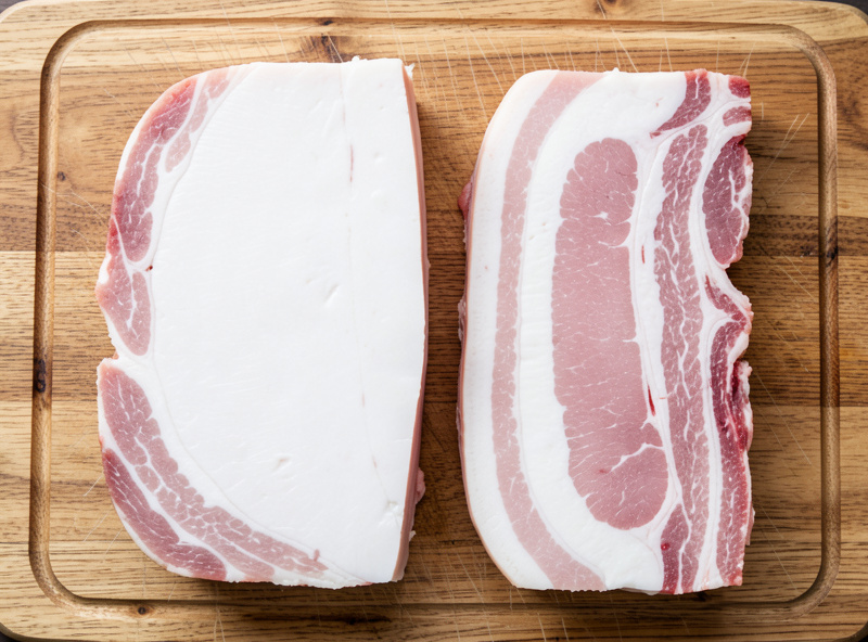 Firm pork back fat next to softer streaky belly fat on a cutting board